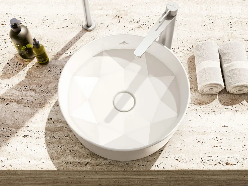 Vasque octogonale blanche sur un plan de travail moucheté Vasque ronde blanche sur un plan de travail moucheté avec robinet, serviettes et distributeur de savon à proximité.