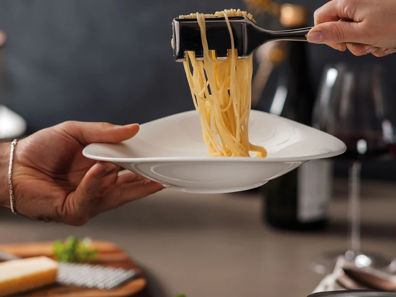 Des pâtes dans une assiette Vapiano de Villeroy & Boch Une assiette Vapiano tenue à la main, des pâtes sont servies avec une pince de Villeroy & Boch.