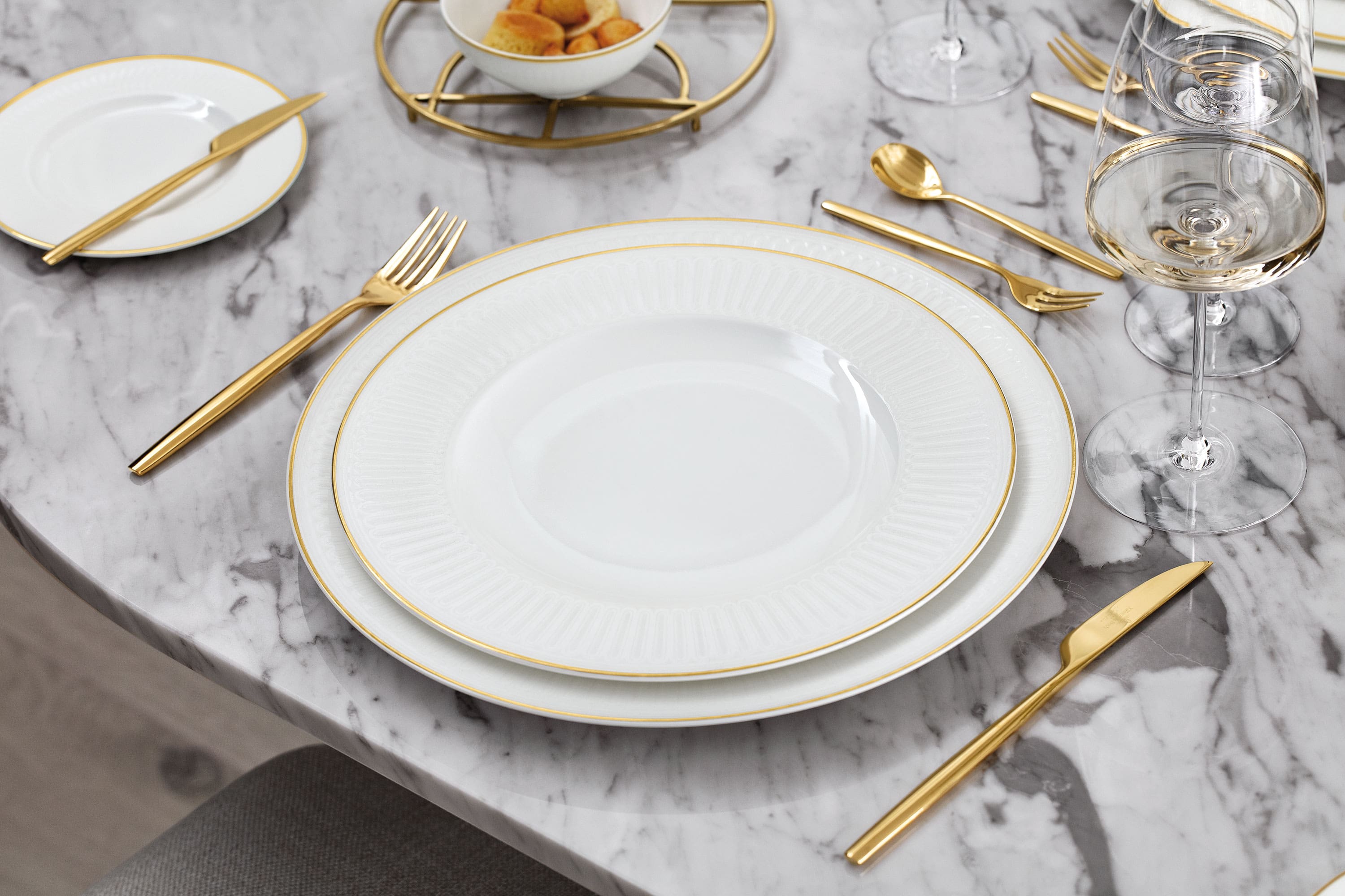 La collection Château Septfontaines dressée sur une table en marbre Un ensemble de vaisselle blanc et doré de Château Septfontaines sur une table en marbre.