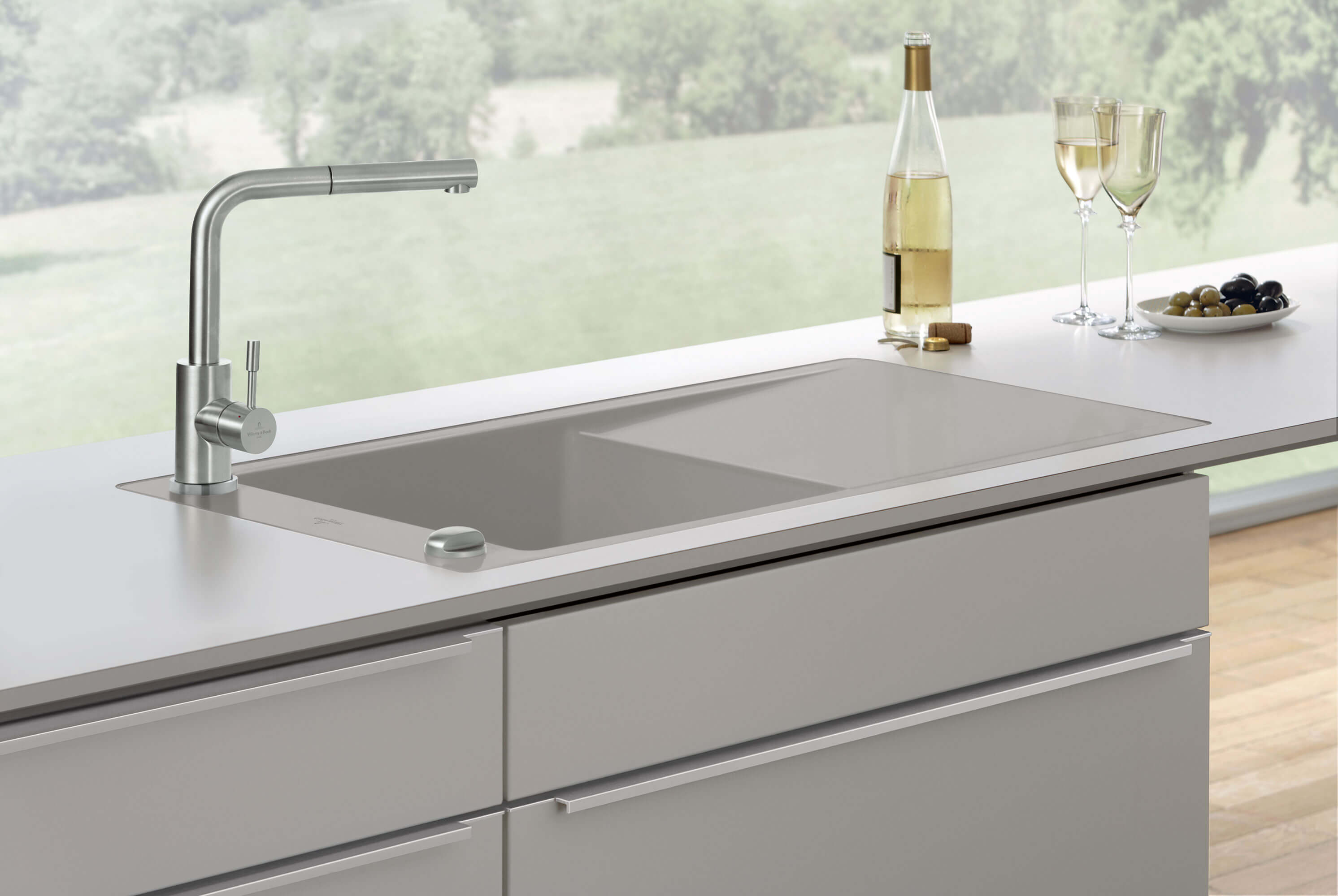 Un évier de cuisine gris Timeline 60 flat à fleur de plan avec une robinetterie dans une cuisine lumineuse avec deux verres à vin, une bouteille de vin et des olives dans une coupe.