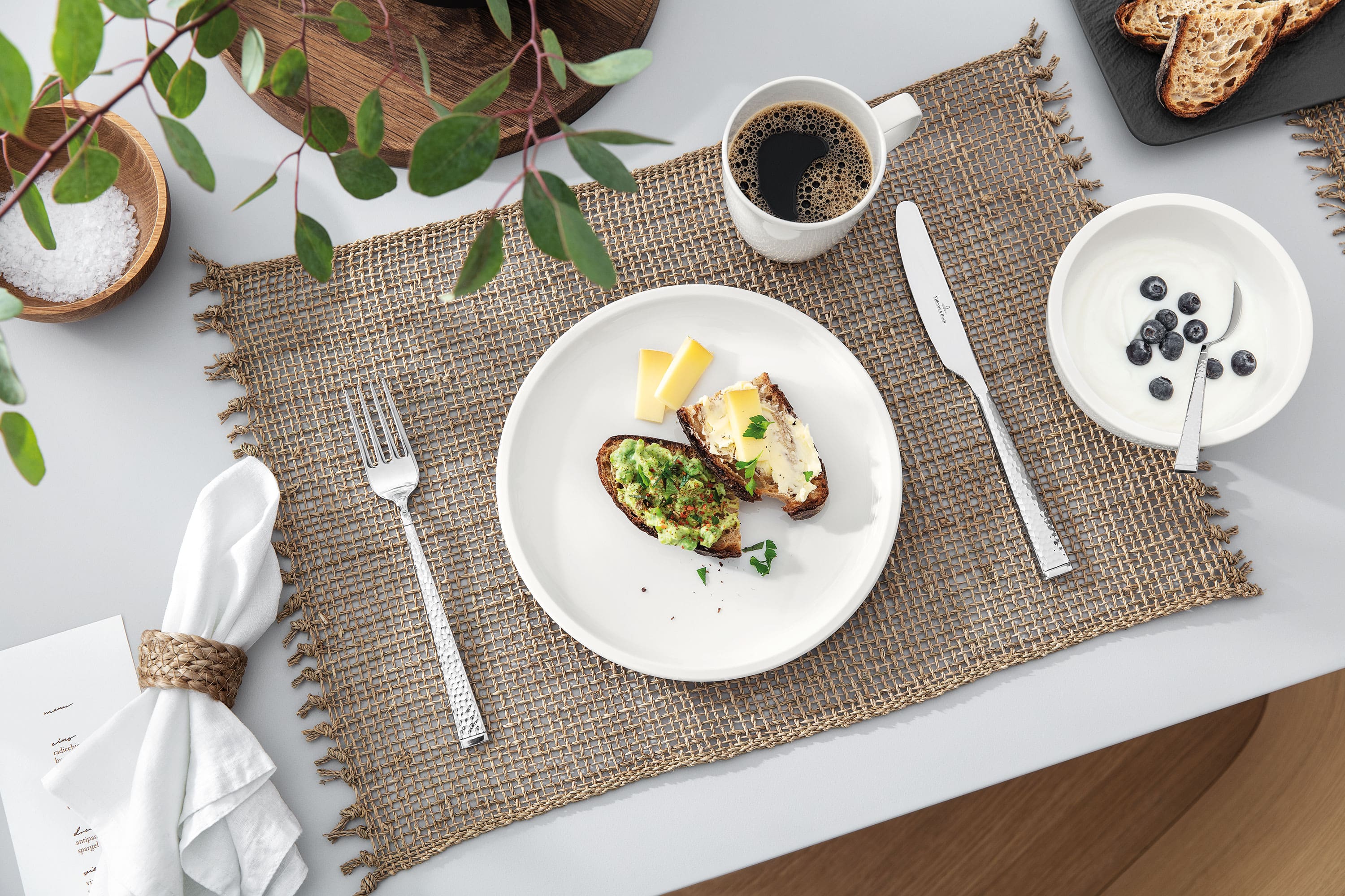 Vaisselle Artesano de Villeroy & Boch disposée sur la table du petit-déjeuner Une table dressée avec une tasse à café et une assiette Artesano blanche de Villeroy & Boch avec de la nourriture.