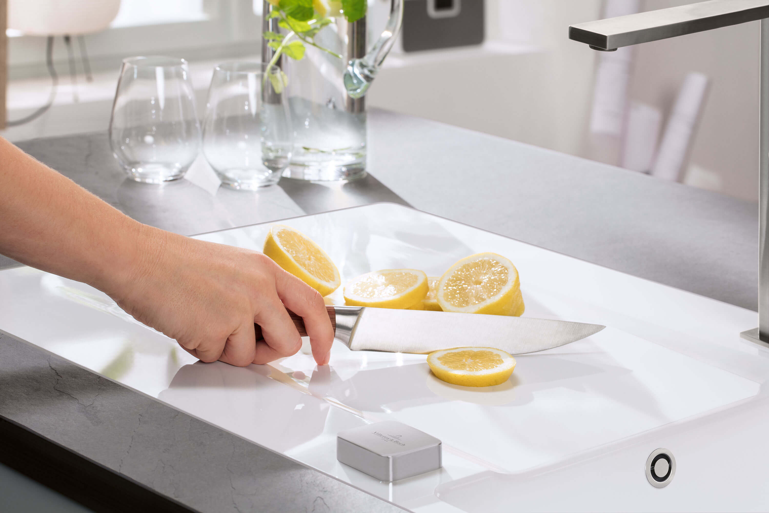 Une personne coupe des citrons dans une cuisine moderne sur un évier de cuisine blanc.
