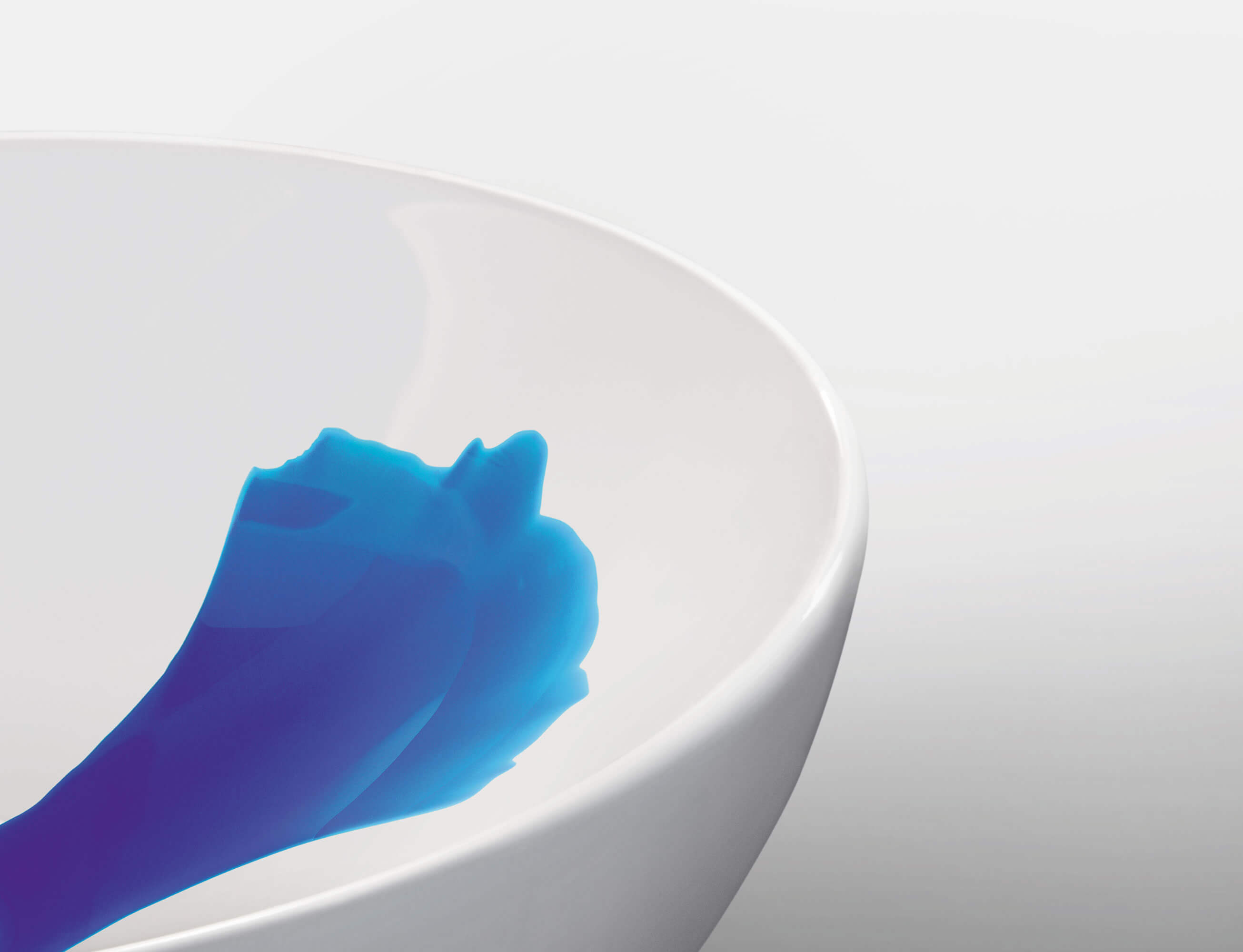 Un lavabo blanc sur le bord duquel s’écoule un liquide bleu en formant un large motif.